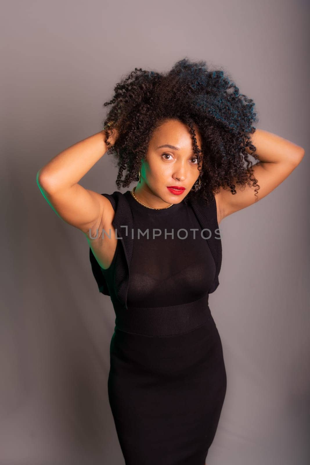 Portrait of beautiful young brunette woman messing with her hair. Dressed in black. Isolated on gray background