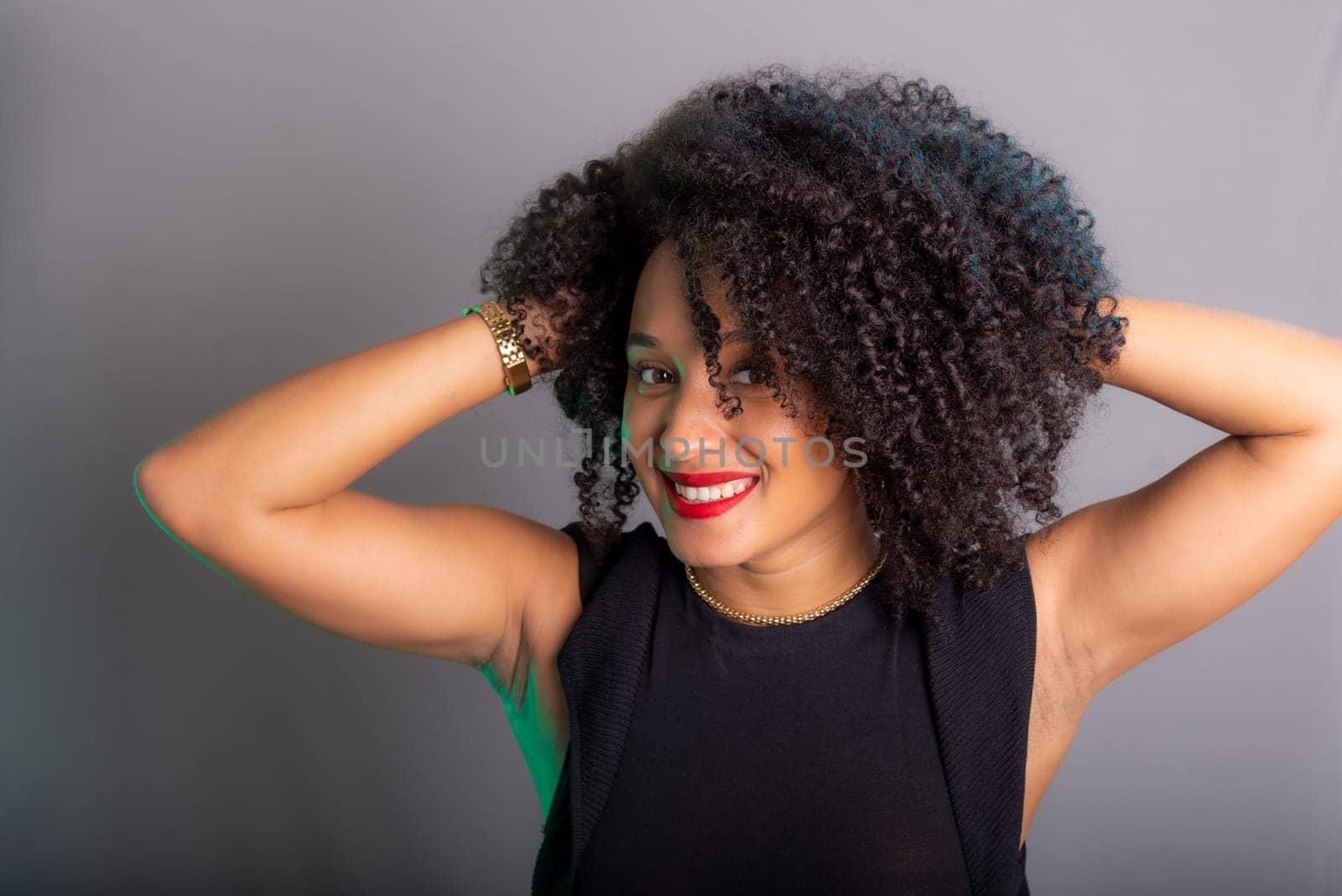 Portrait of beautiful young brunette woman messing with her hair. Dressed in black. Isolated on gray background