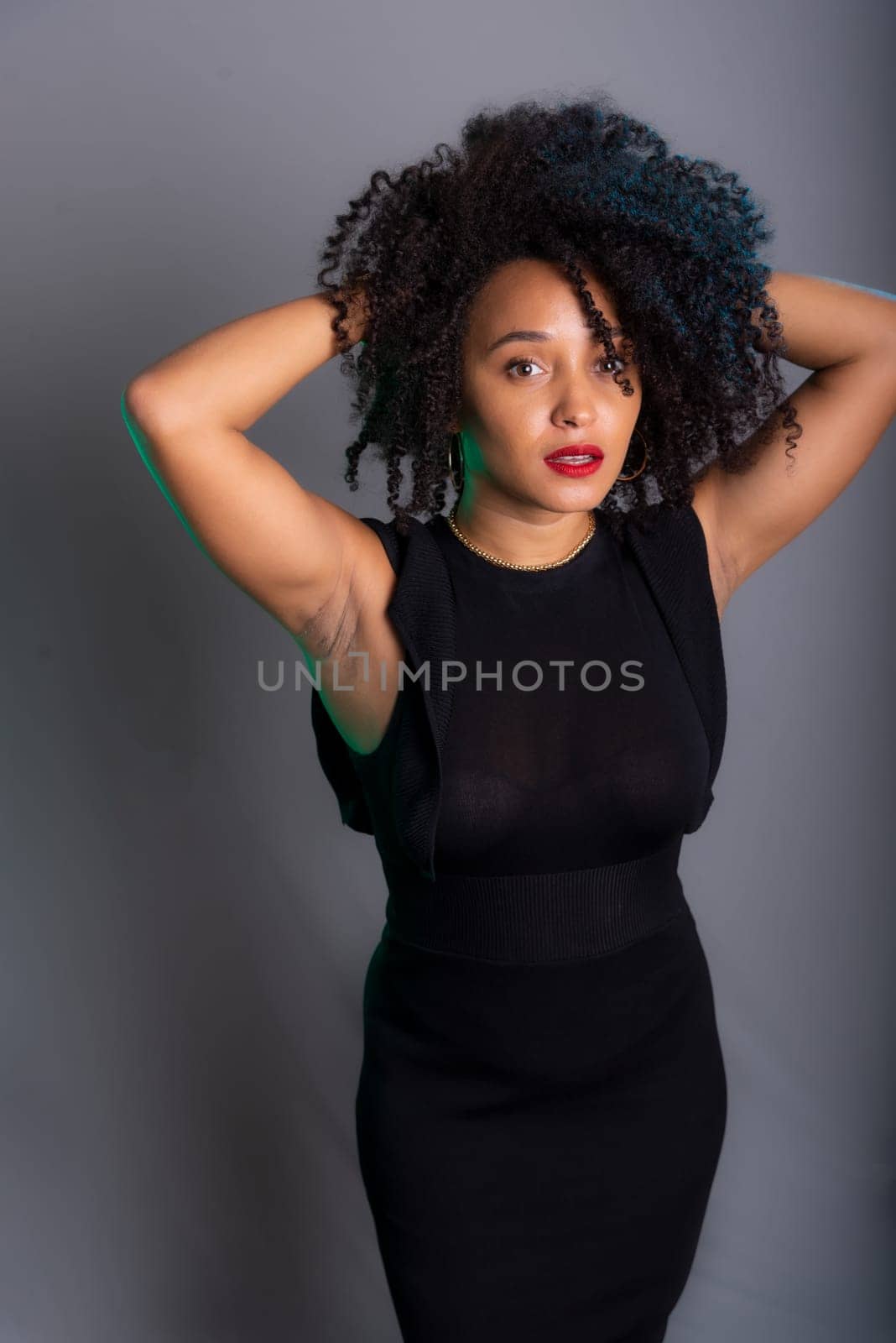 Portrait of beautiful young brunette woman messing with her hair. Dressed in black. Isolated on gray background