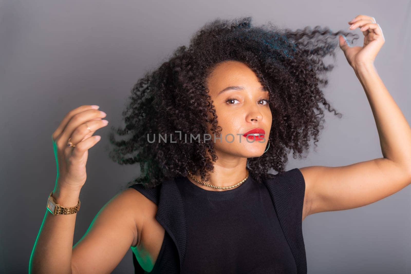 Portrait of beautiful young brunette woman messing with her hair. Dressed in black. Isolated on gray background