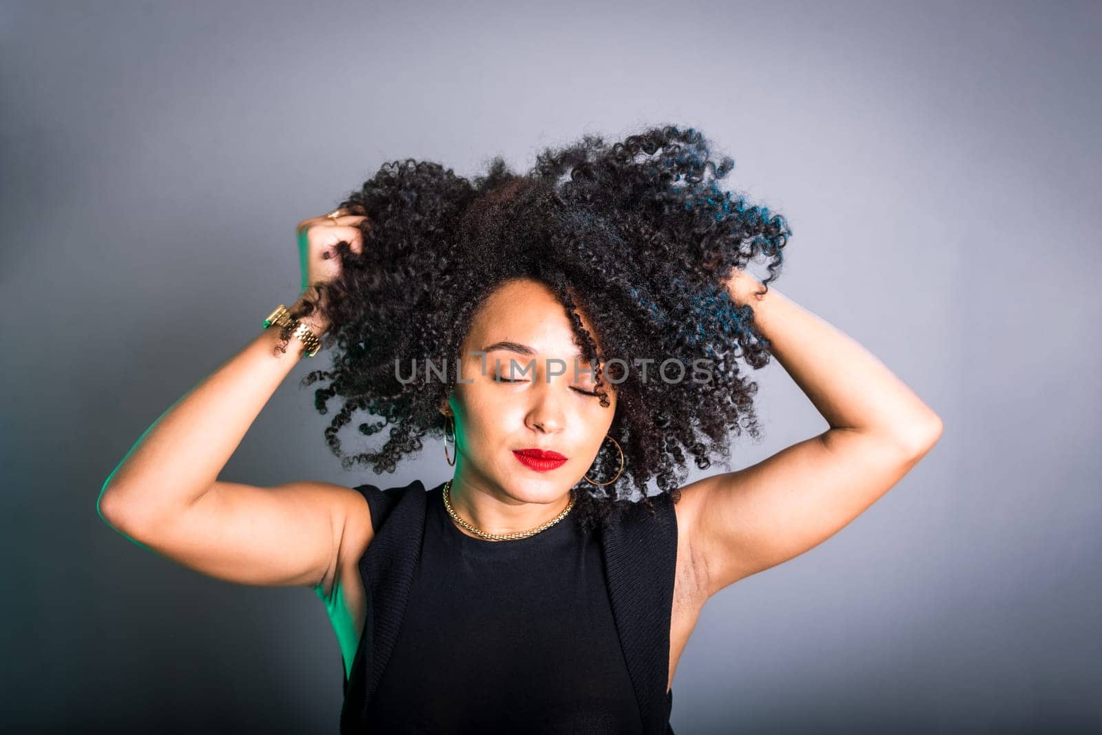 Portrait of beautiful young brunette woman messing with her hair. Dressed in black. Isolated on gray background