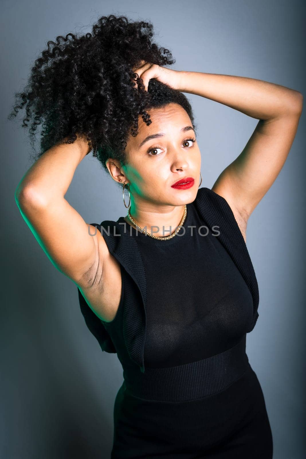Beautiful young woman standing against gray background messing with her black hair. studio portrait