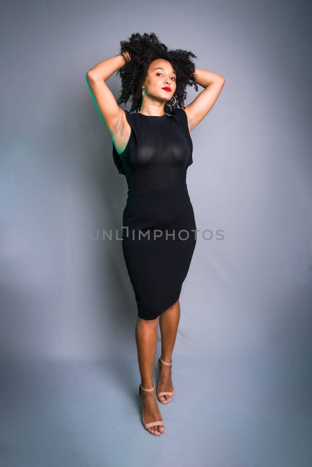 Beautiful young woman standing against gray background messing with her black hair. studio portrait