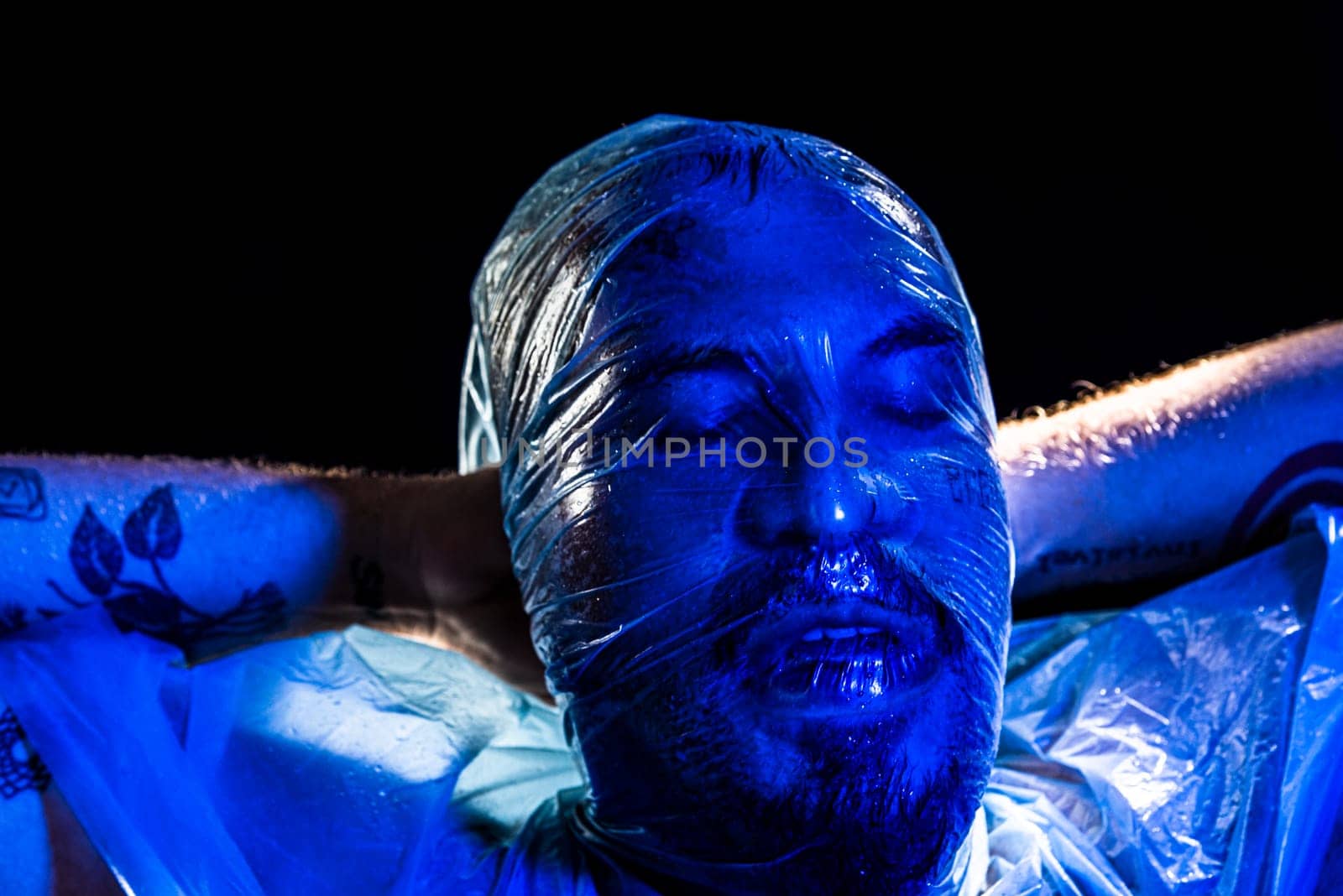 Man with plastic bag over his head, suffocated. Studio shot with blue filter. Isolated on black background.