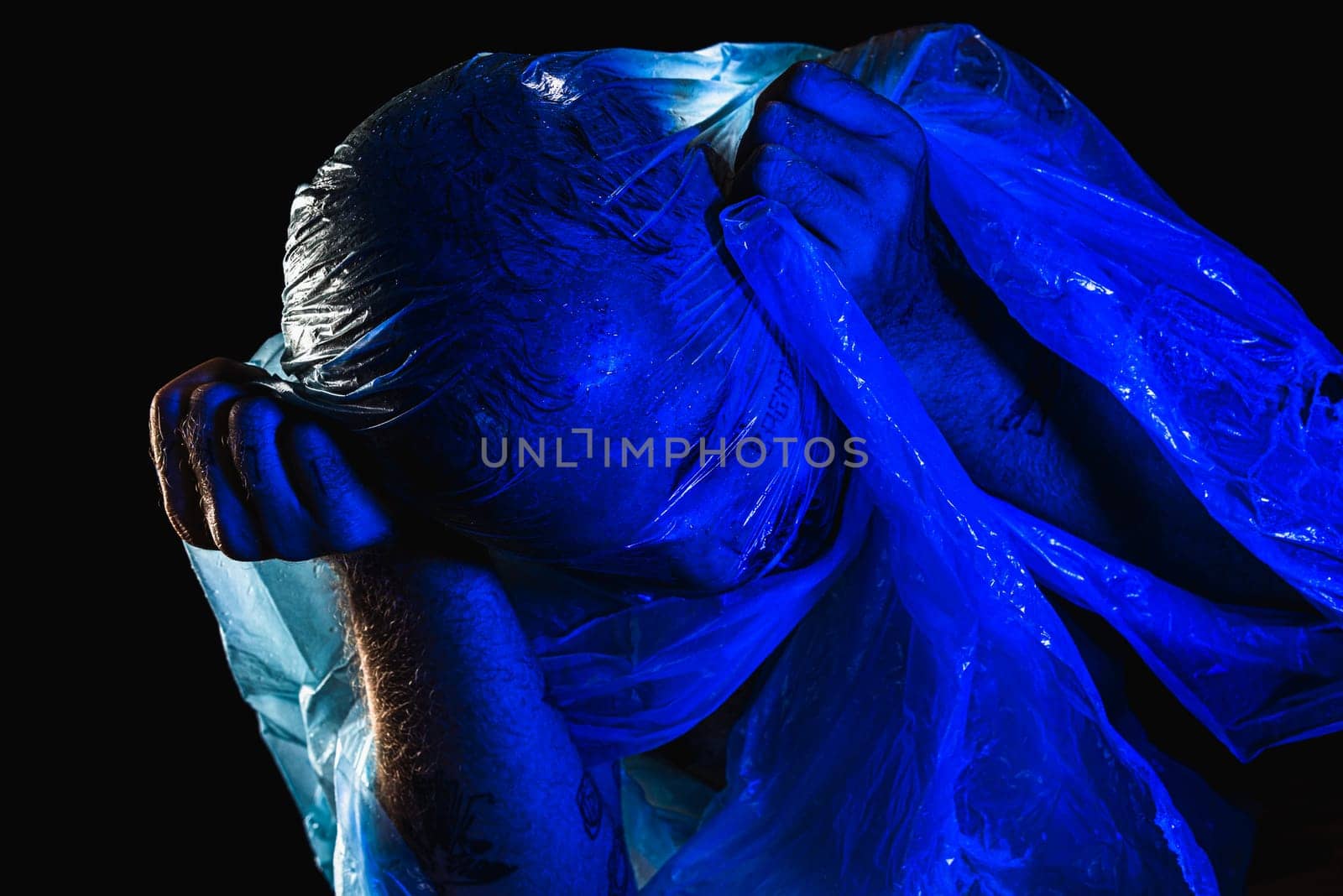 Man with plastic bag over his head, suffocated. Studio shot with blue filter. Isolated on black background.