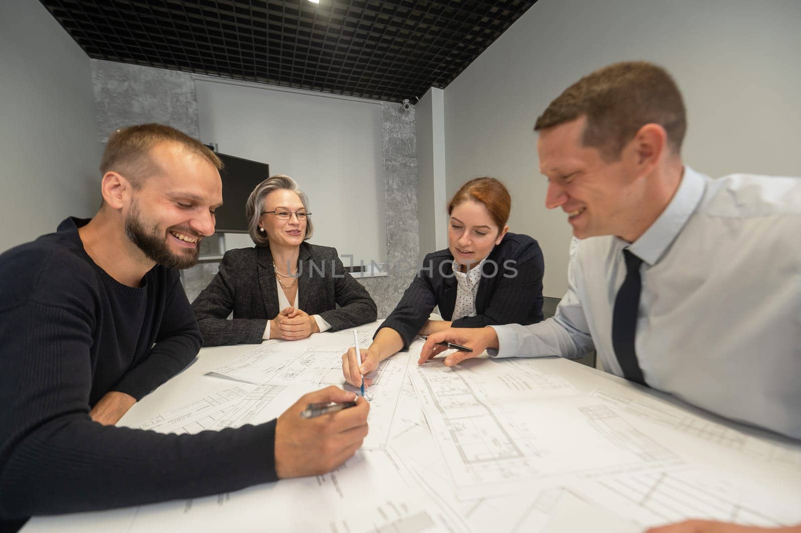 Four business people sitting around a table discussing blueprints. Designers engineers at a meeting. by mrwed54