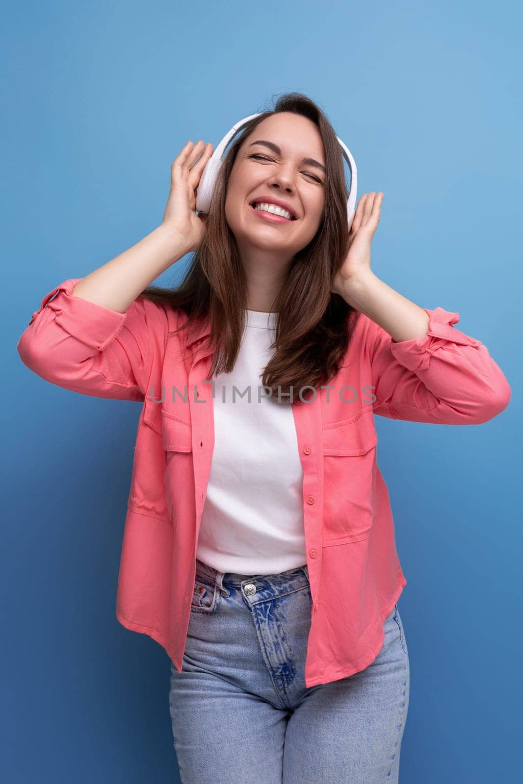 enjoying brunette young woman with dark hair below her shoulders in a shirt and jeans with wireless headphones.