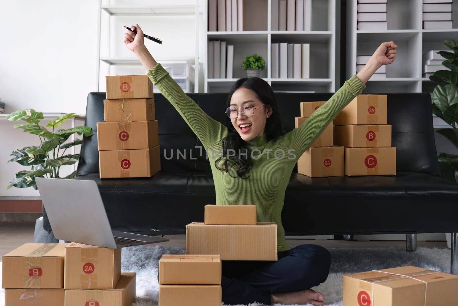 Happy young Asian woman entrepreneur, Smile for sales success after checking order from online shopping store in a laptop at home office, Concept of merchant business online by nateemee