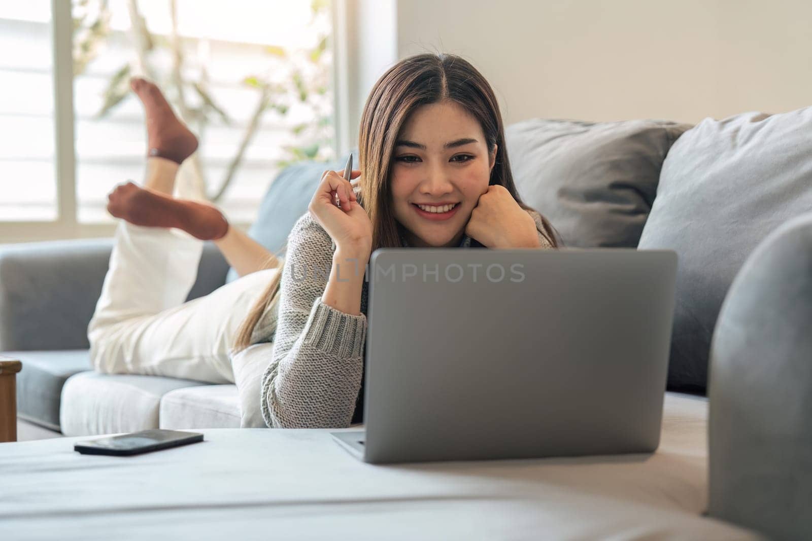 Young woman relaxing using laptop computer on a cold winter day in the bedroom. woman checking social apps and working. Communication and technology concept by nateemee