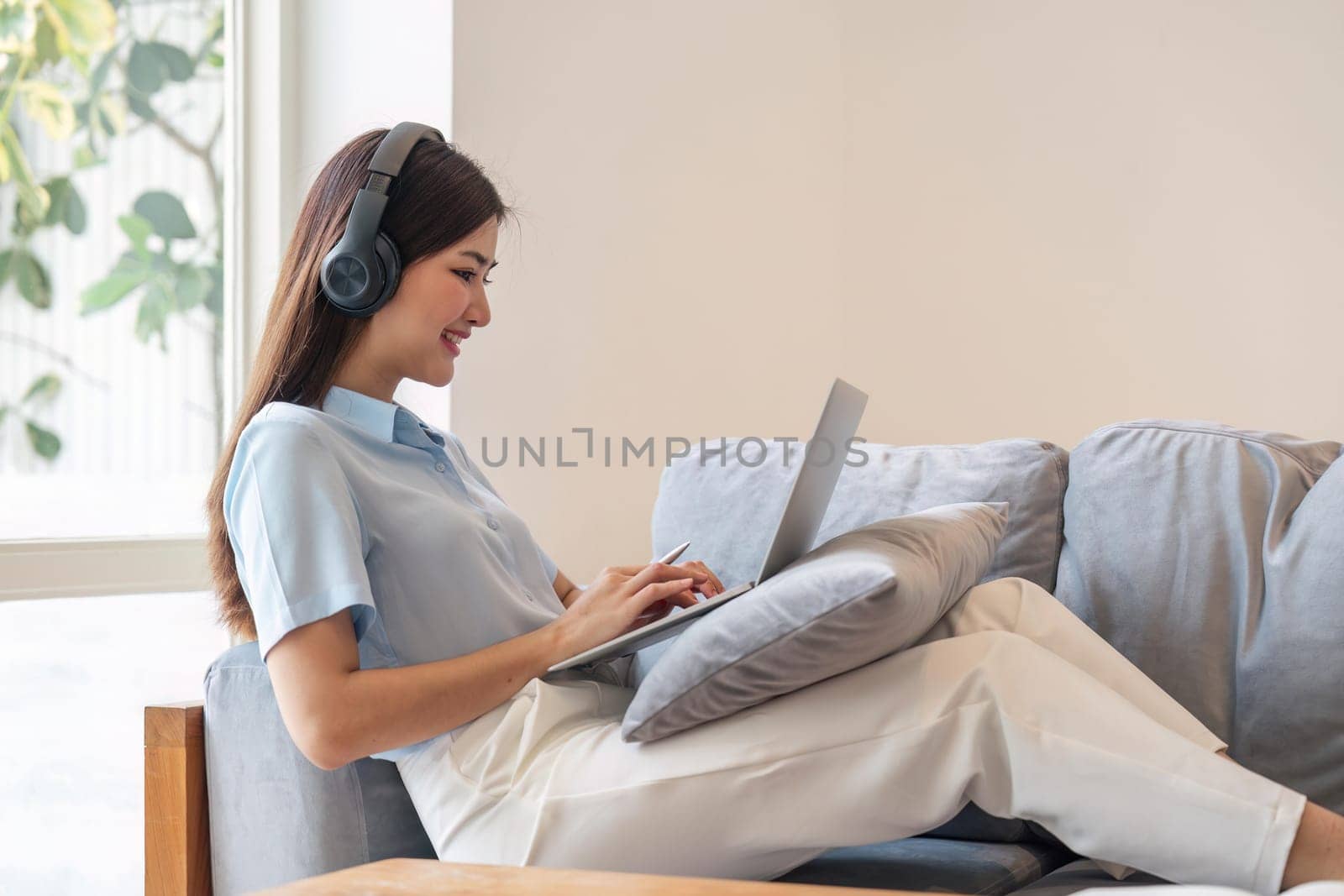Image of smiling happy beautiful asian woman relaxing using of laptop computer while sitting on desk woman creative girl working at home concept by nateemee