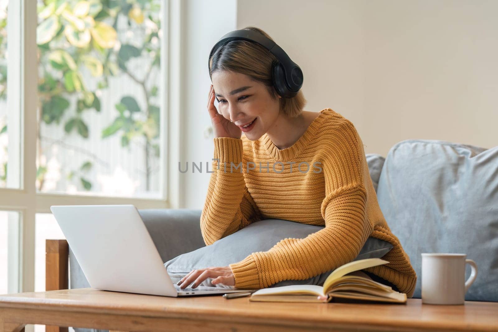 Young Asian woman wear headphone and enjoy with music via music app on laptop by nateemee