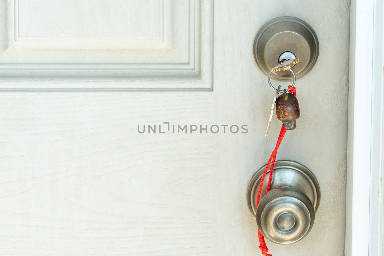 A key with a keychain on a red rope is inserted into the door lock.