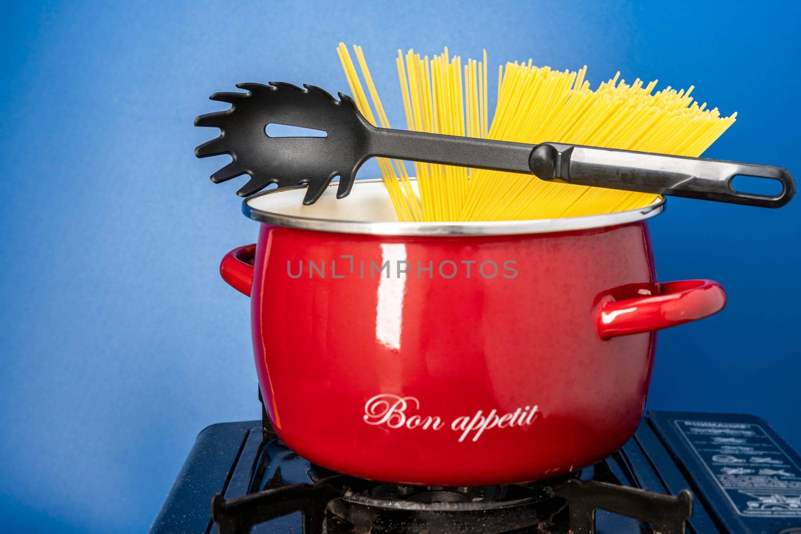 we cook ourselves. spaghetti in a saucepan. a beautiful red saucepan with spaghetti and skimmer. cooking spaghetti in a saucepan on a gas stove. homemade Italian-style dinner. kitchen saucepan on a blue background