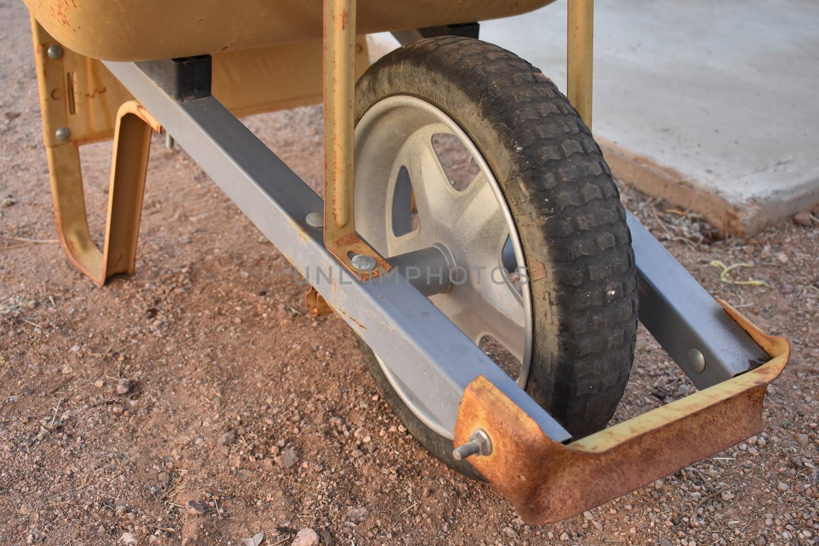 Wheel on Bottom of Orange Wheelbarrow on Dirt Ground. High quality photo