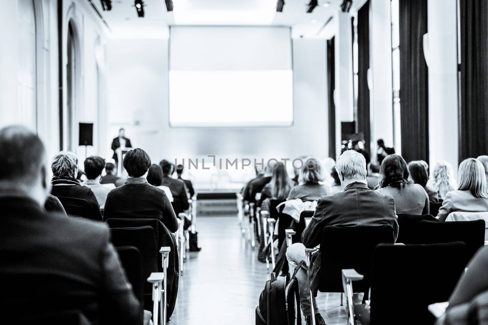 Speaker giving a talk in conference hall at business event. Rear view of unrecognizable people in audience at conference hall. Business and entrepreneurship concept. Black and white selenium image.