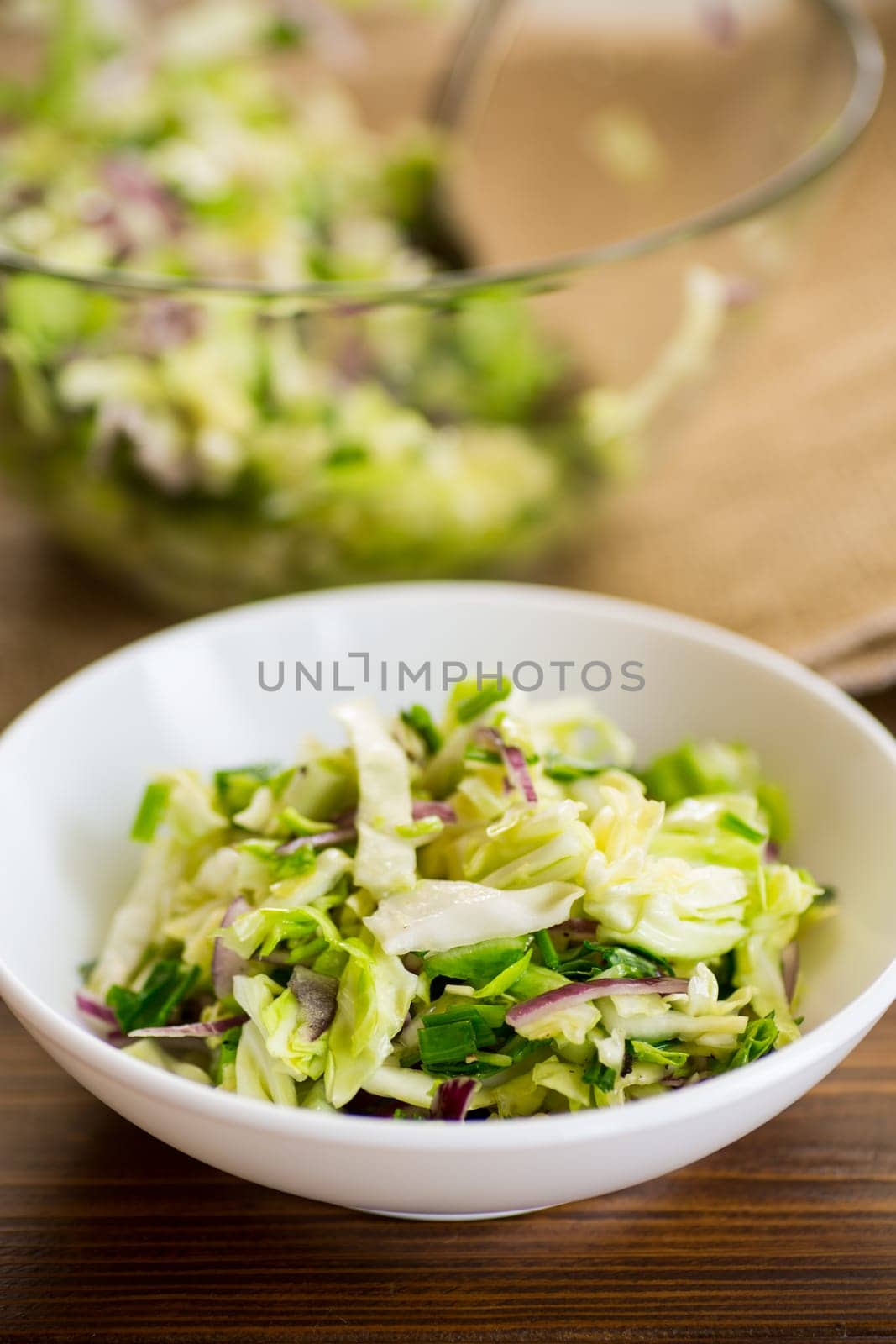 Young cabbage salad with purple onions in a bowl on a wooden table.