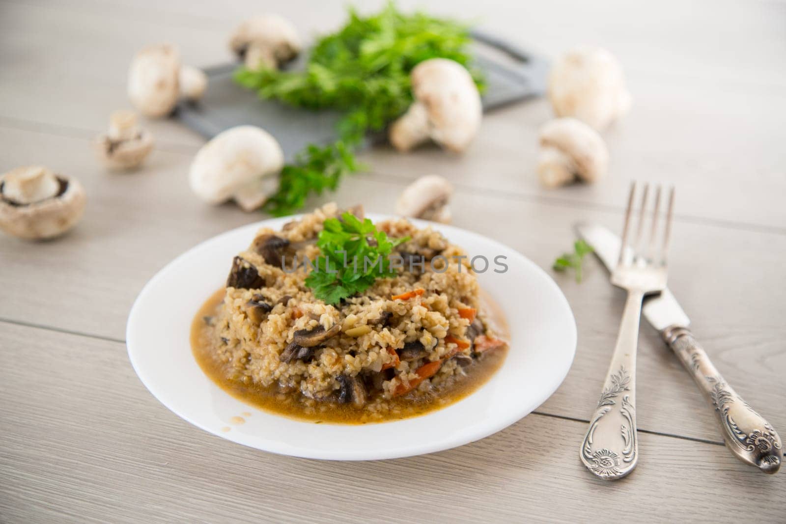 cooked bulgur with mushrooms, carrots and vegetables in a plate, on a wooden table.