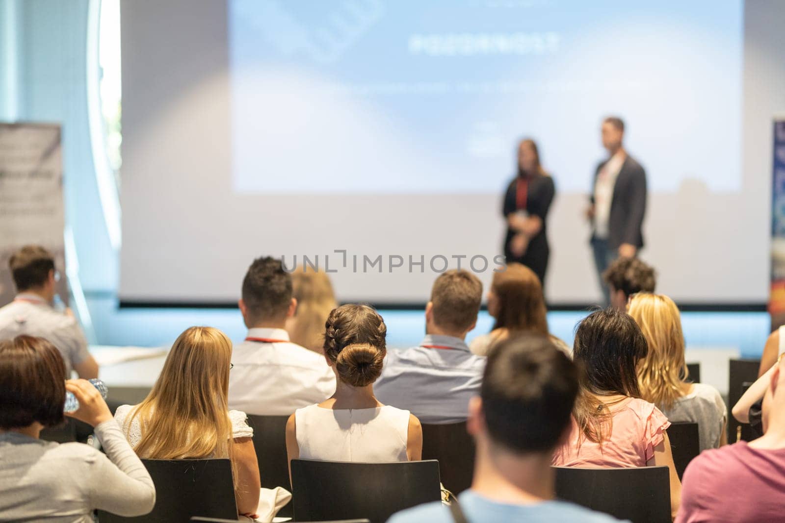 Startup team giving a pitch deck presentation in conference hall at business event. Audience at the conference hall. Business and Entrepreneurship concept. Focus on unrecognizable people in audience.