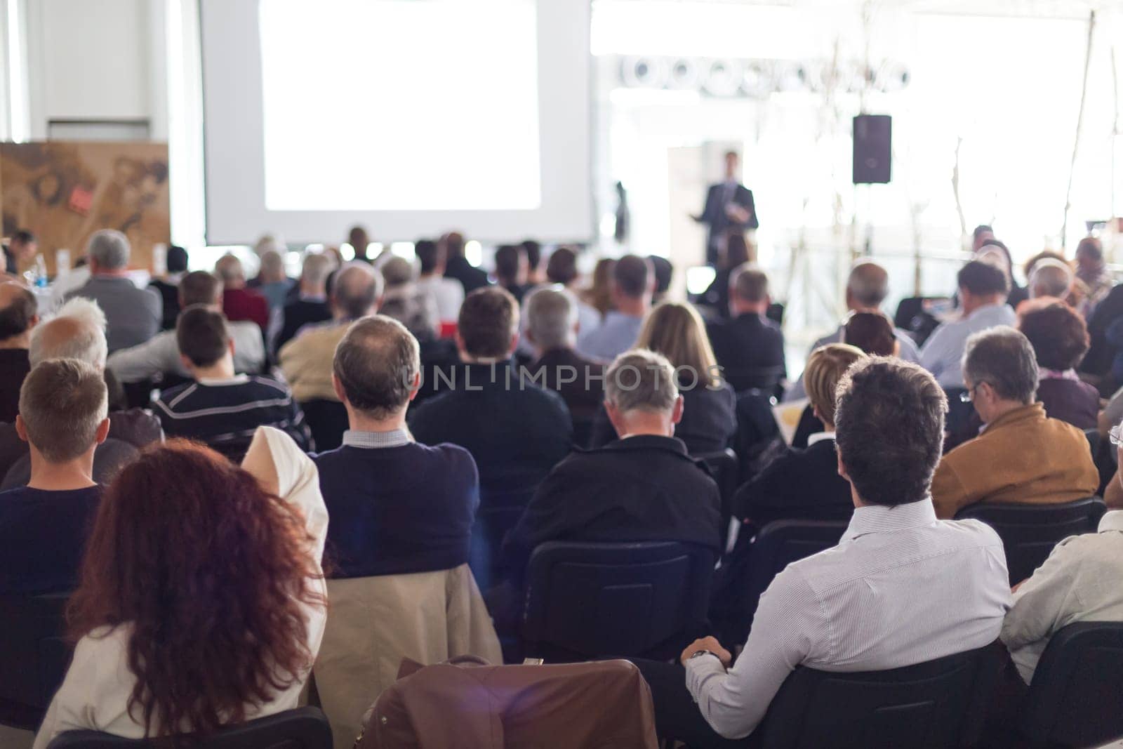 Speaker giving a talk in conference hall at business event. Audience at the conference hall. Business and Entrepreneurship concept. Focus on unrecognizable man in the audience.