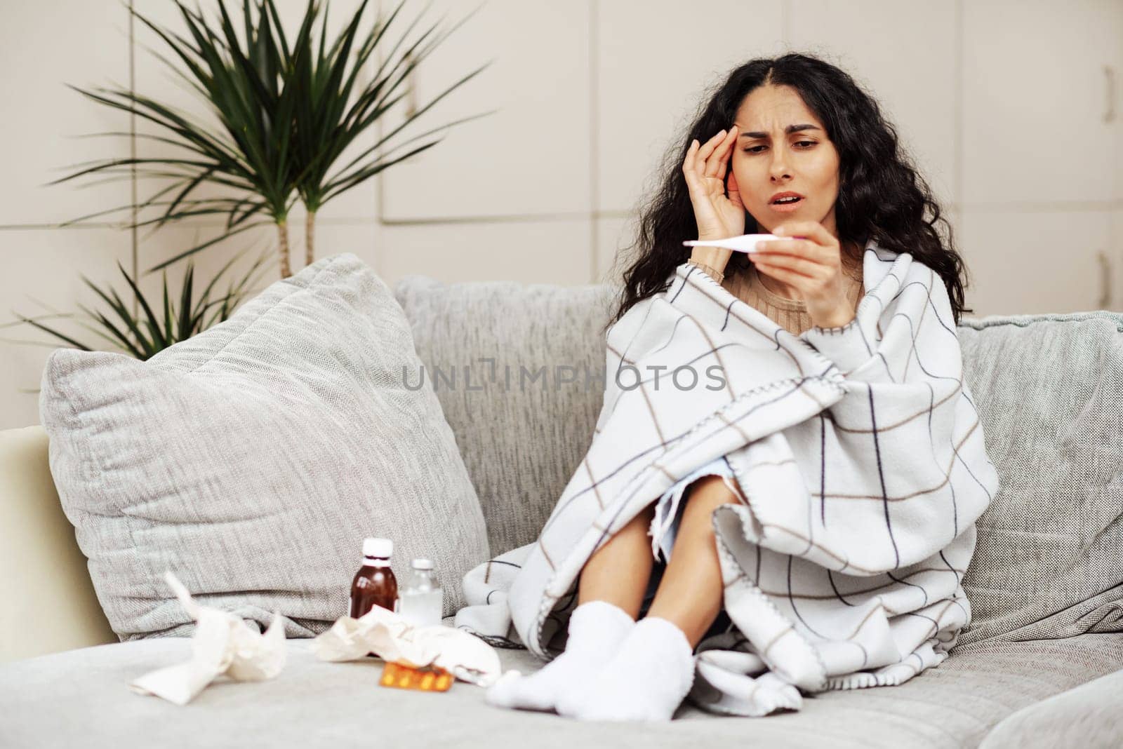 Young woman looks at the thermometer with horror. A beautiful young woman of Arab appearance came home from work and noticed a high body temperature. She has a long treatment ahead of her, which scares and worries her. Unexpected illness leads to disorder.