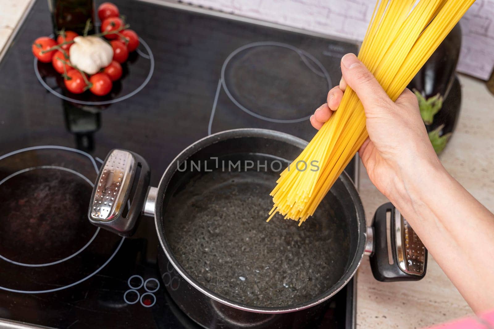 Closeup of spaghetti in pot on stove. the cook's hand drops the spaghetti into a saucepan of boiling water. Pasta cooking