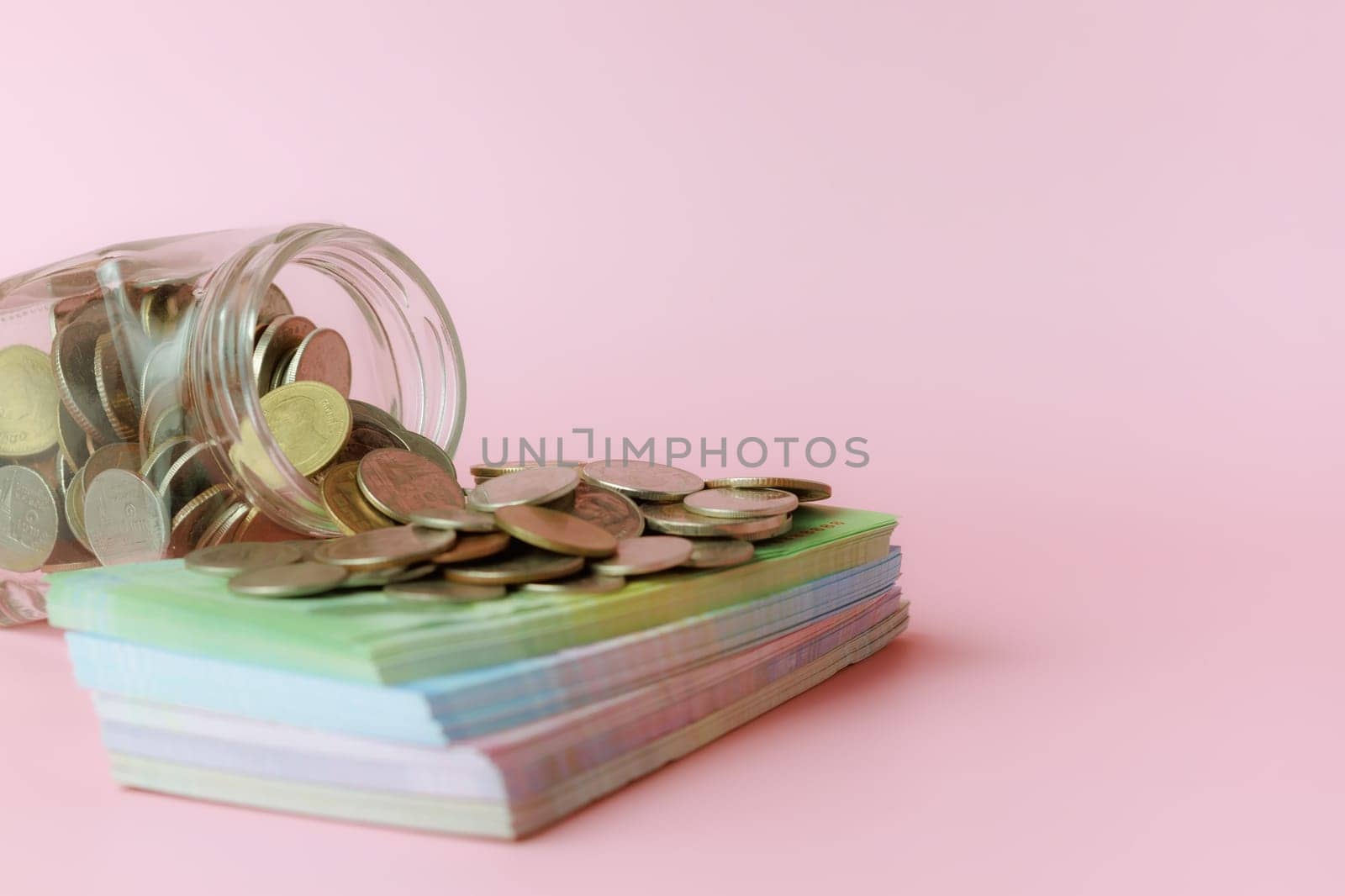 A glass jar of coins with banknotes on pink background for the concept of business and finance.