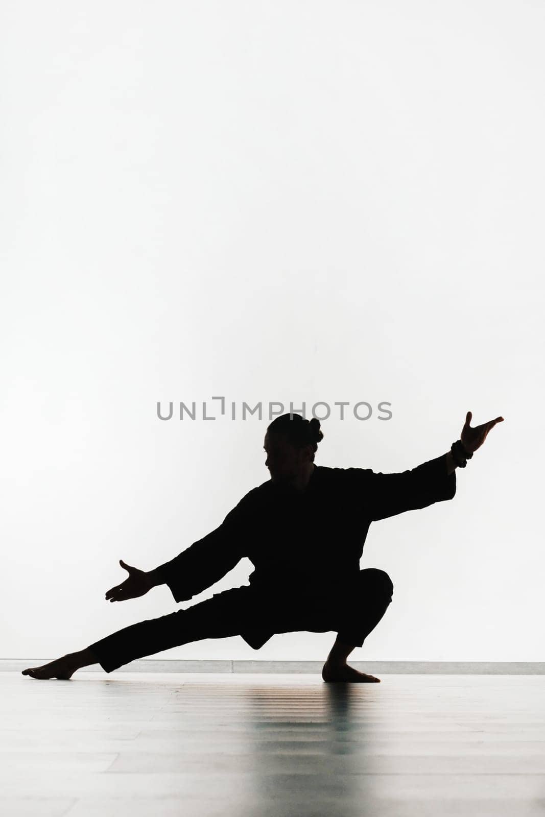 Silhouette of a person practicing qigong energy exercises on a light background.