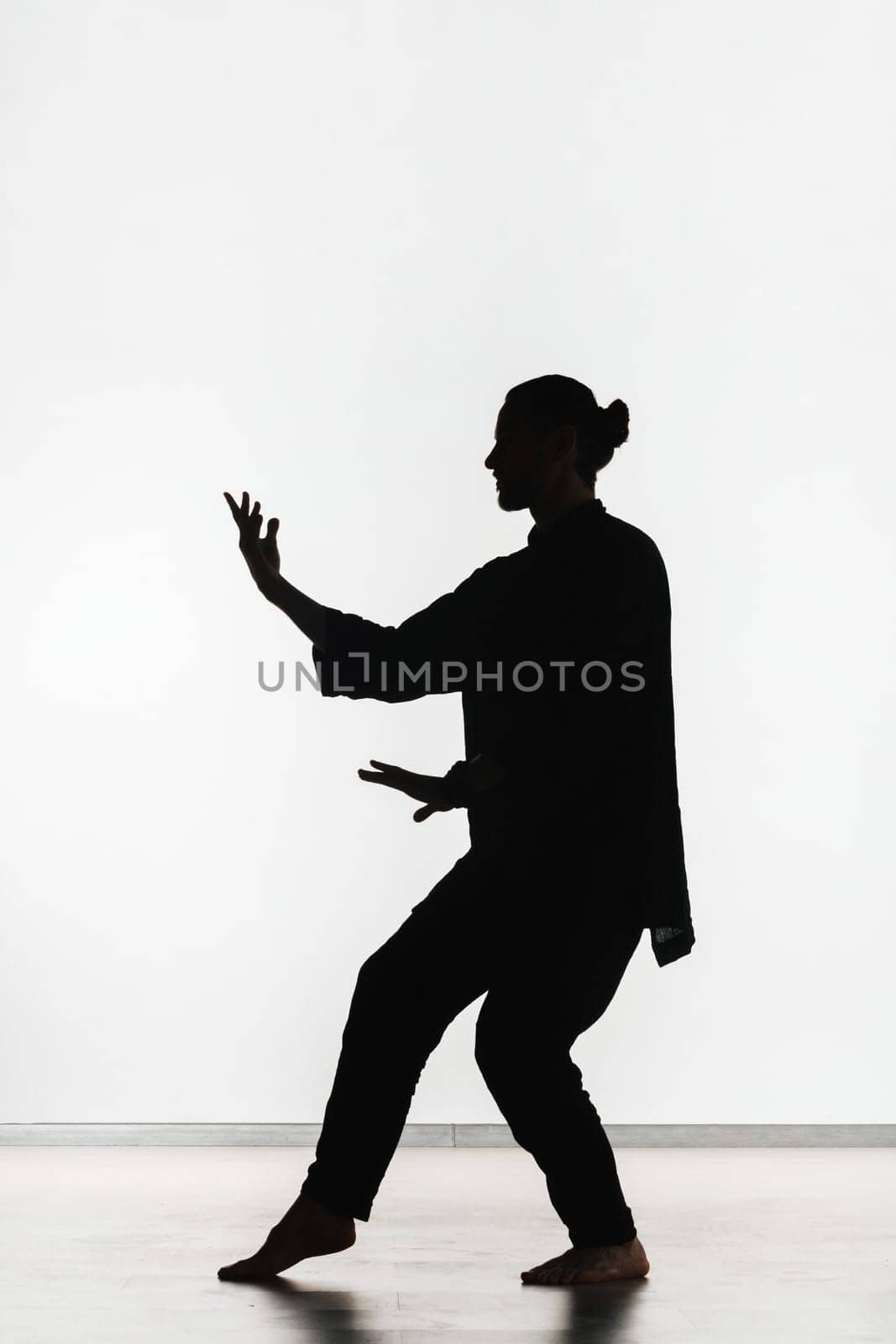 Silhouette of a person practicing qigong energy exercises on a light background.