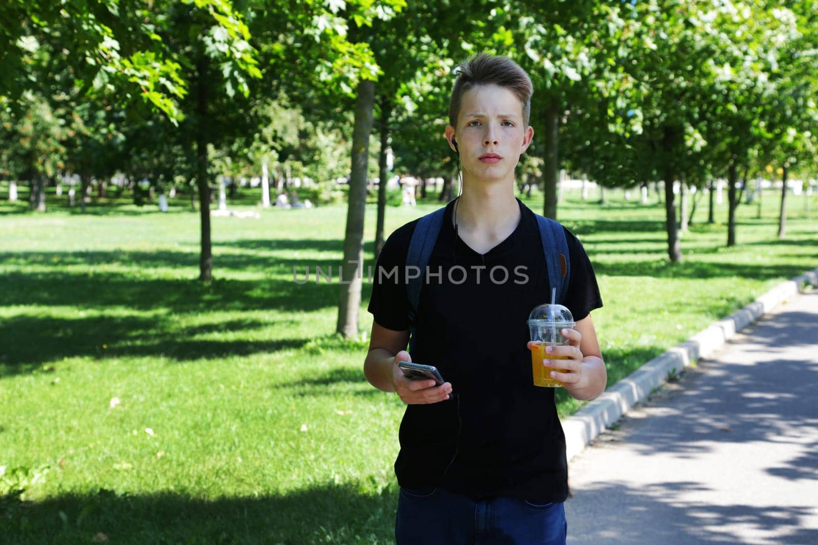 Portrait of a teenager boy with a phone and a plastic glass. by gelog67