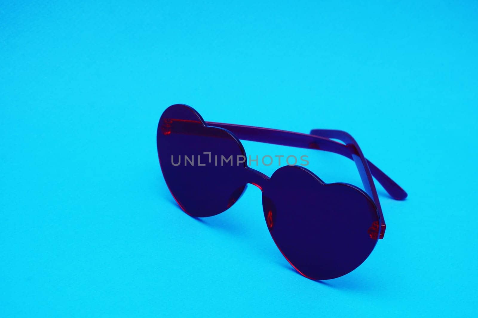 Heart-shaped glamor glasses in dark red color in the shape of a heart on a blue paper background.