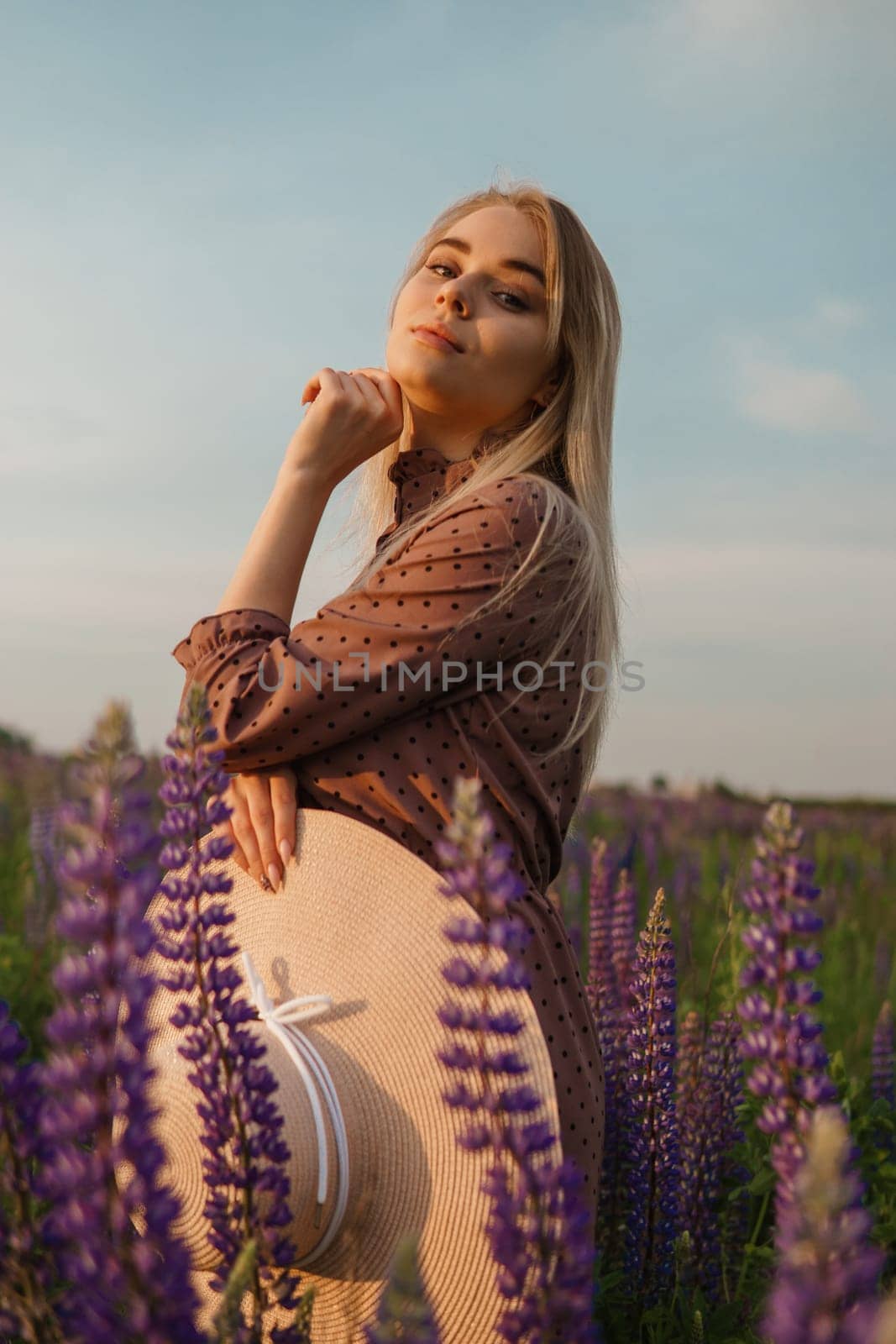 A beautiful woman in a straw hat walks in a field with purple flowers. A walk in nature in the lupin field by Annu1tochka