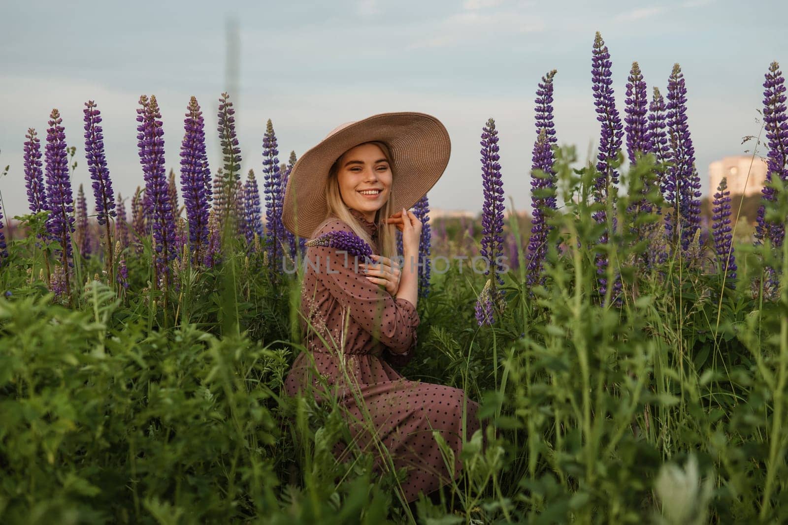A beautiful woman in a straw hat walks in a field with purple flowers. A walk in nature in the lupin field by Annu1tochka