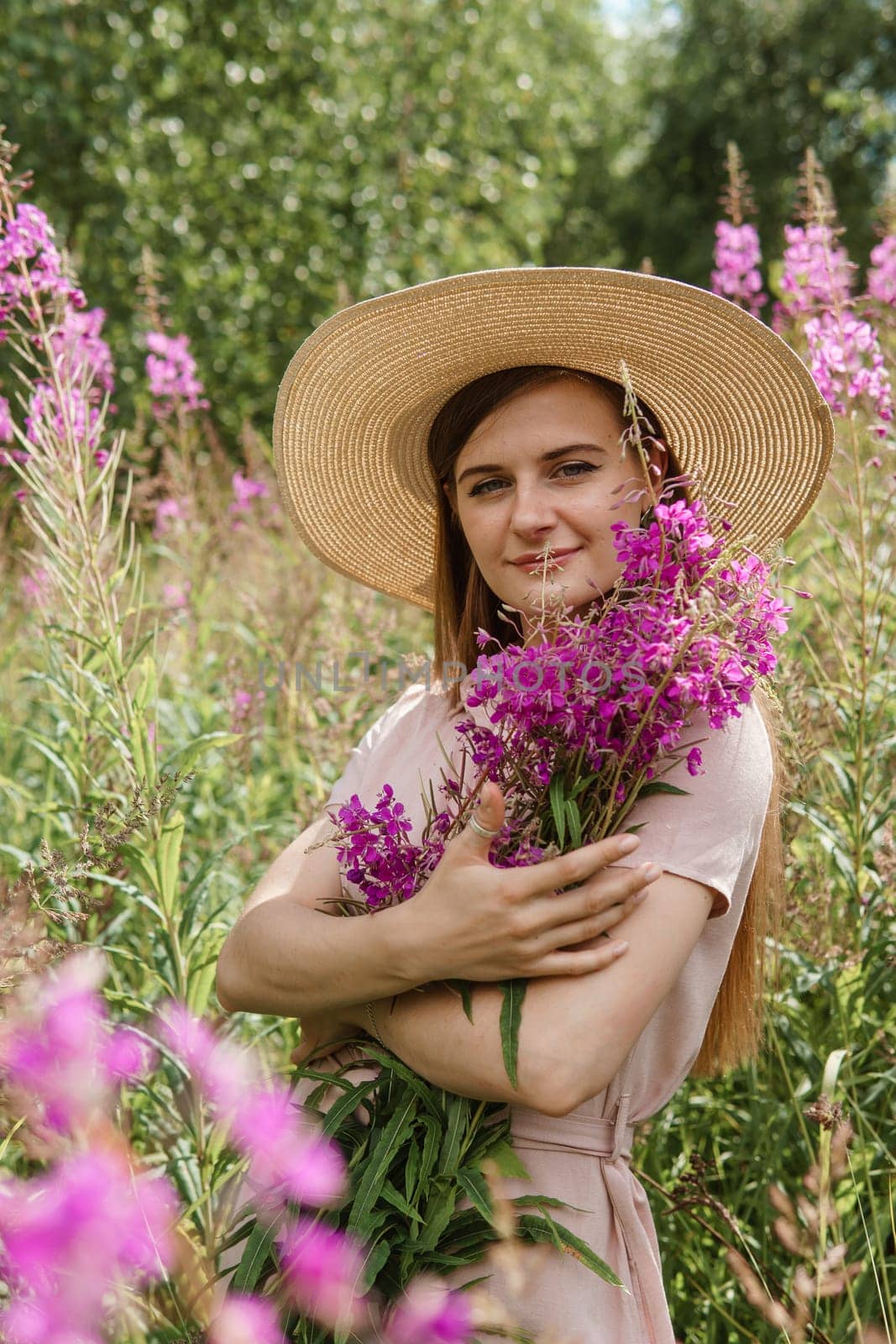 A young woman in nature with a bouquet of pink wild flowers. A bouquet of Ivan-tea in the hands of a woman.