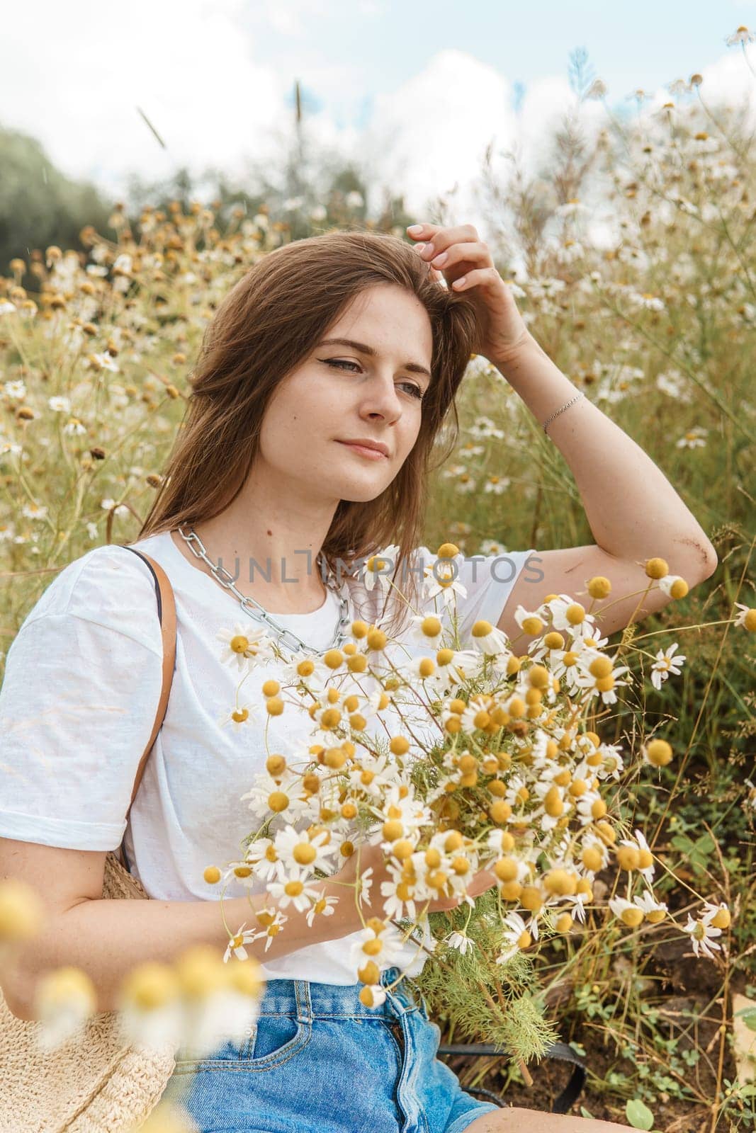 Beautiful young woman in nature with a bouquet of daisies. Field daisies, field of flowers. Summer tender photo.