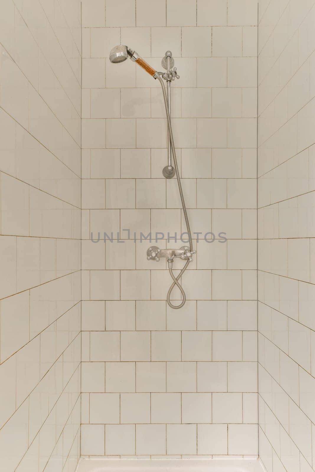 a shower with white tiles on the wall behind it and an orange brush in the corner of the shower head