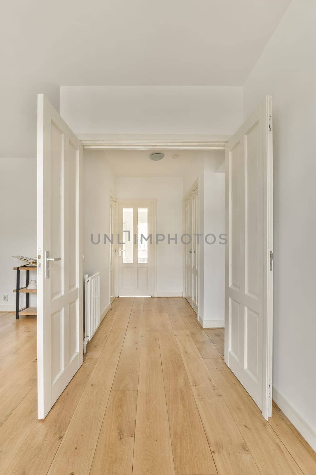 an empty room with white walls and wood flooring on the right side, there is a door leading to another room