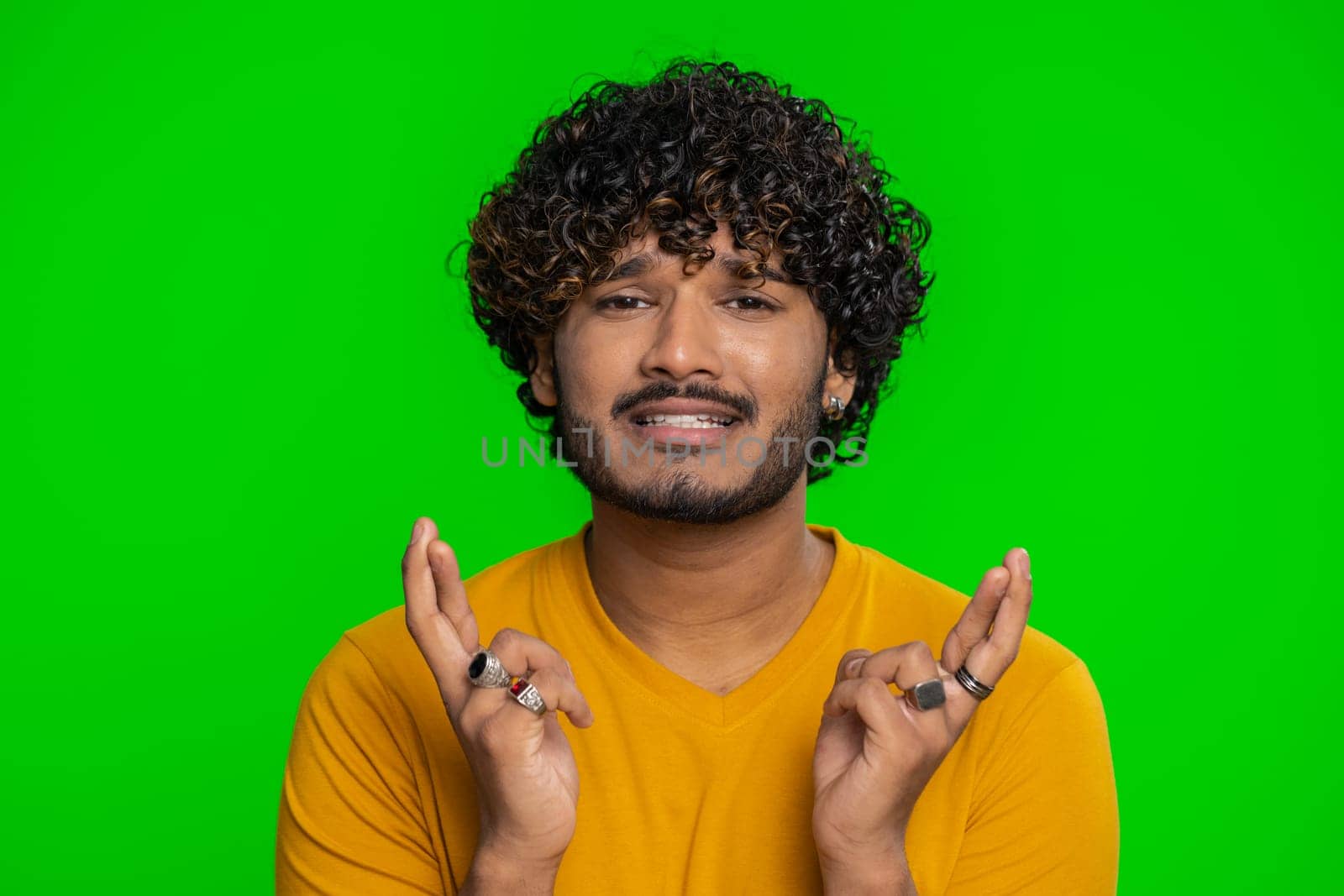 Indian young man crossed fingers looking at camera asking for good lucky news, wishing good exam results, dreaming about win victory in lottery jackpot. Hindu guy isolated on chroma key background
