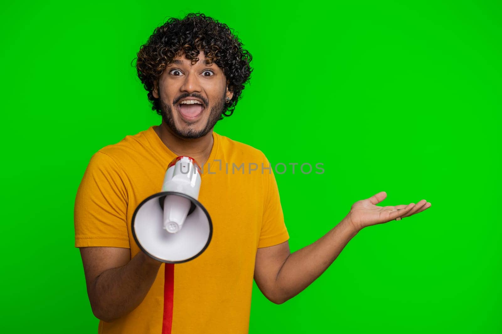 Indian man talking with megaphone, proclaiming news, loudly announcing advertisement, warning using loudspeaker to shout speech, pointing empty place. Copy-space. Handsome guy on chroma key background