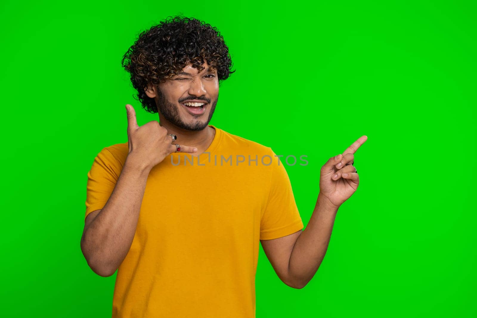 Call us, here is contact number. Handsome bearded indian man in shirt looking at camera doing phone gesture like says hey you call me back conversation. Hindu guy isolated on chroma key background