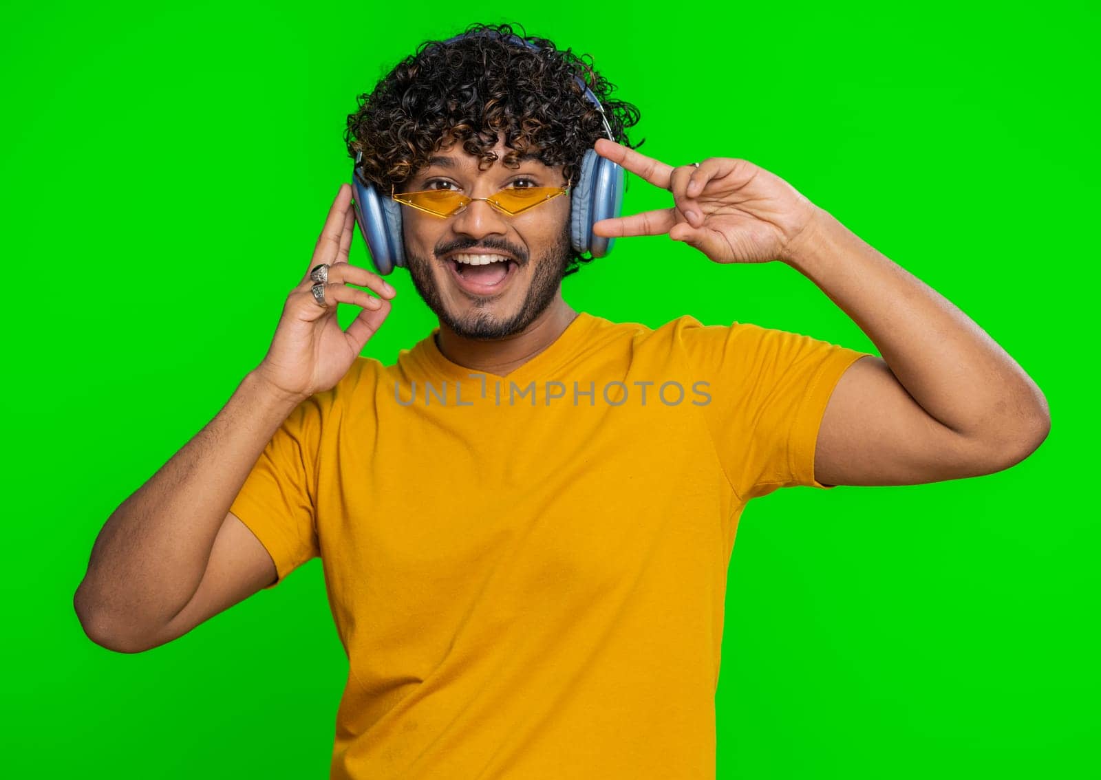 Happy indian man in headphones listening music and dancing disco fooling around having fun expressive gesticulating hands, relaxing on party. Hindu guy isolated alone on studio chroma key background