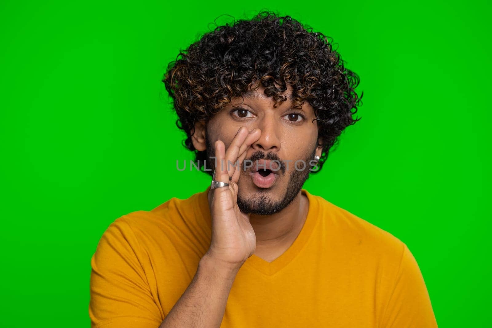 Keep my secrets, silence. Indian man whisper news rumors holding hands near mouth, share gossip, quiet. Hindu guy telling interesting confidential story isolated on green chroma key background indoors