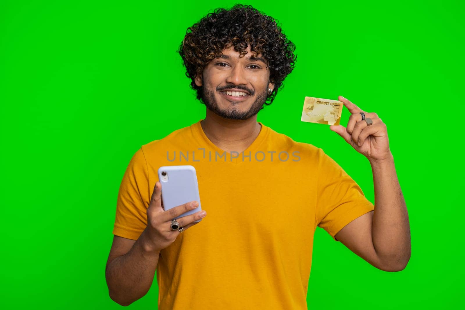 Sincere indian man customer using credit bank card and smartphone while transferring money, purchases online shopping, payment. Finance and internet. Handsome guy isolated on chroma key background