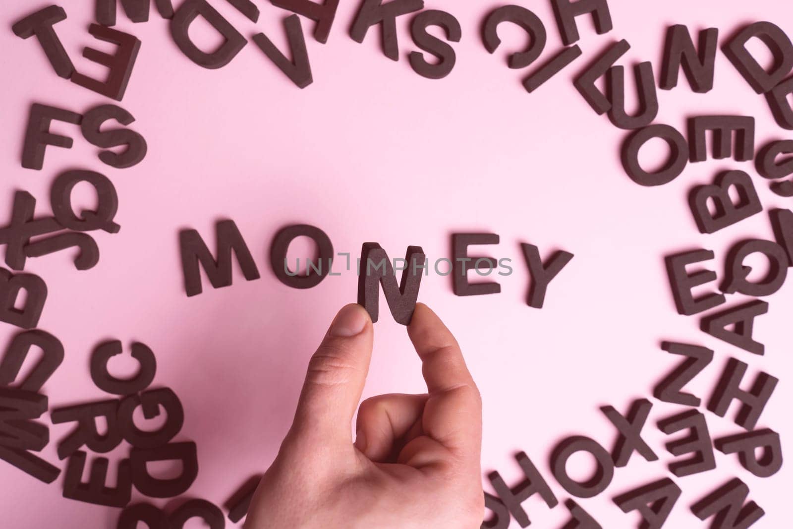 A man's hand holds the letter n, collects the word money from letters on a light pink background, a financial concept on the topic of savings, needs, salaries.