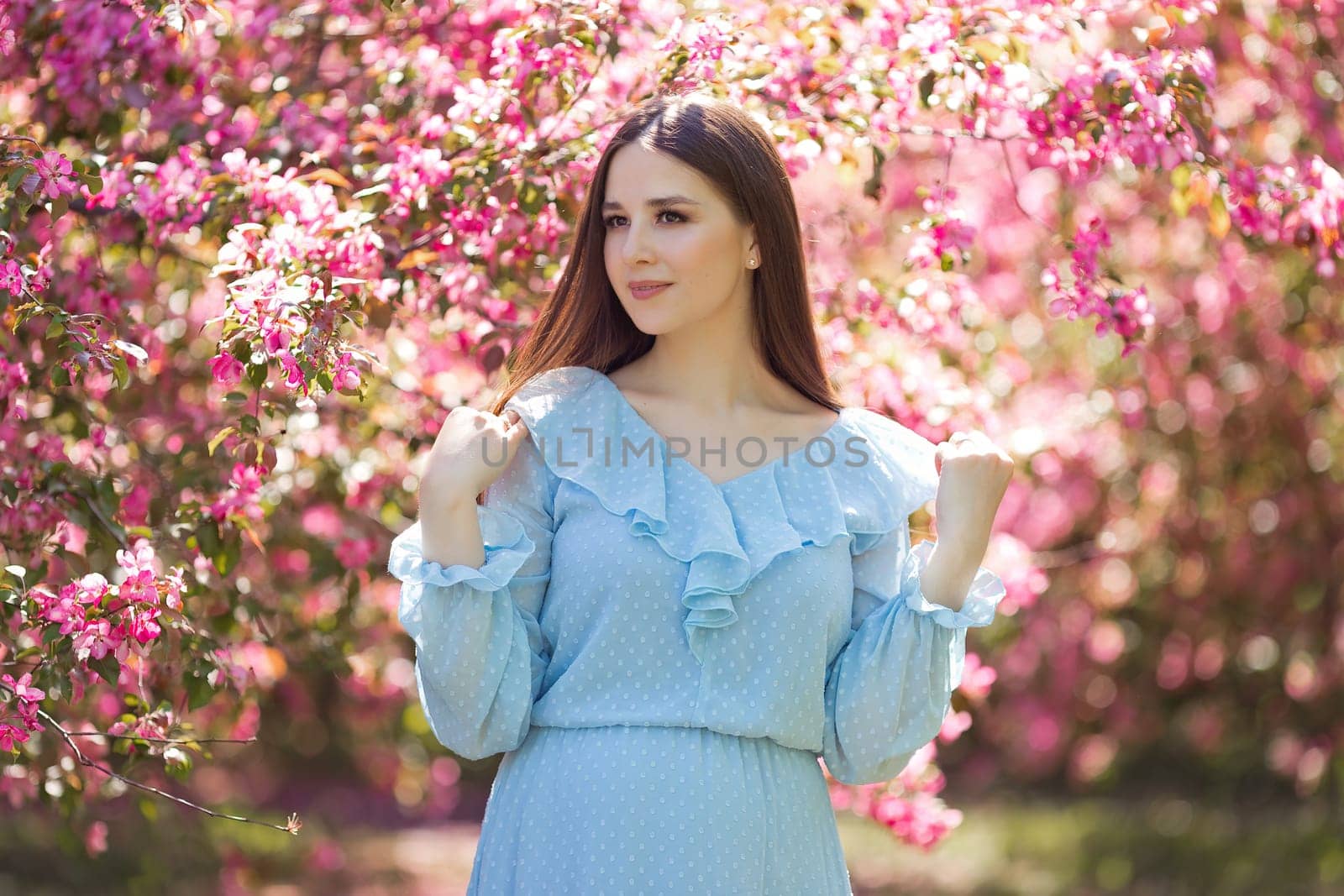 A beautiful girl long hair is stands in a pink blooming garden s. Close up