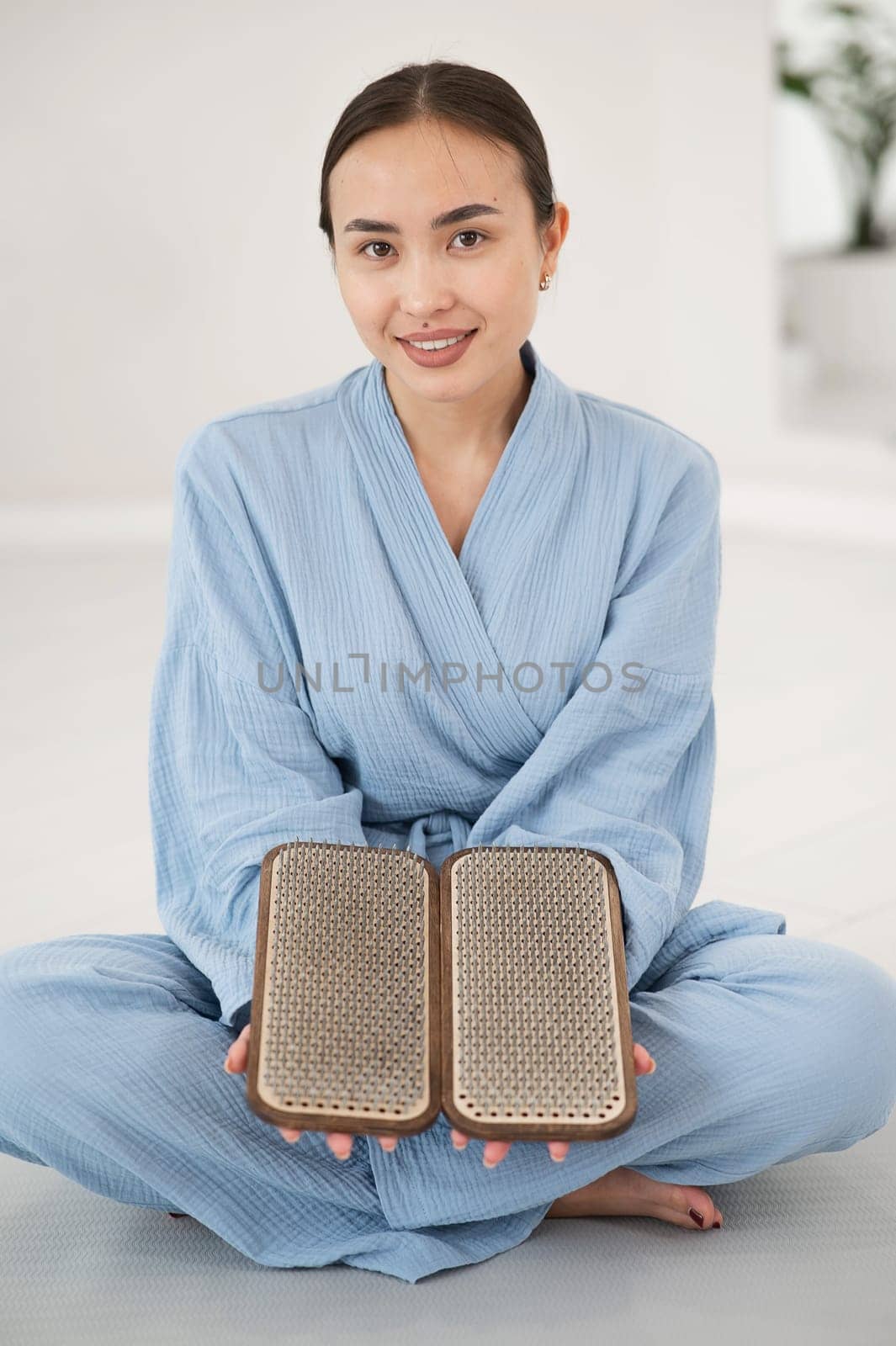 Asian woman sitting in lotus position on yoga mat and holding sadhu boards