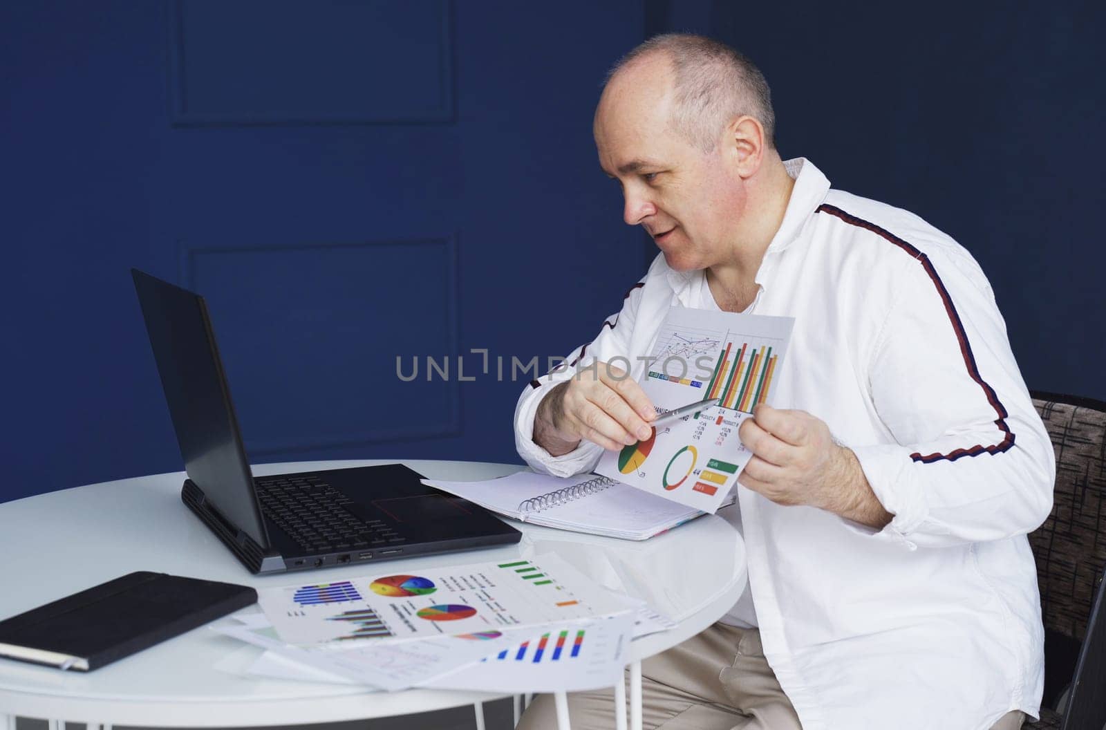 A man makes an online video call chat, sitting at home and talking into a laptop webcam, showing a document.