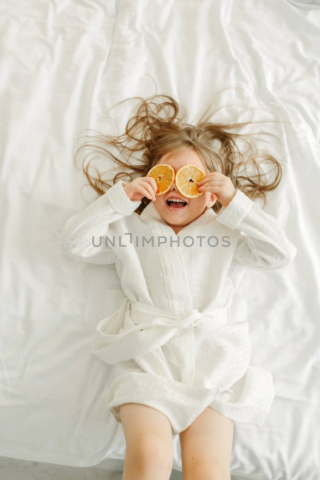 A young girl in a white coat, lying in bed, playing with candied oranges, closed her eyes with them.