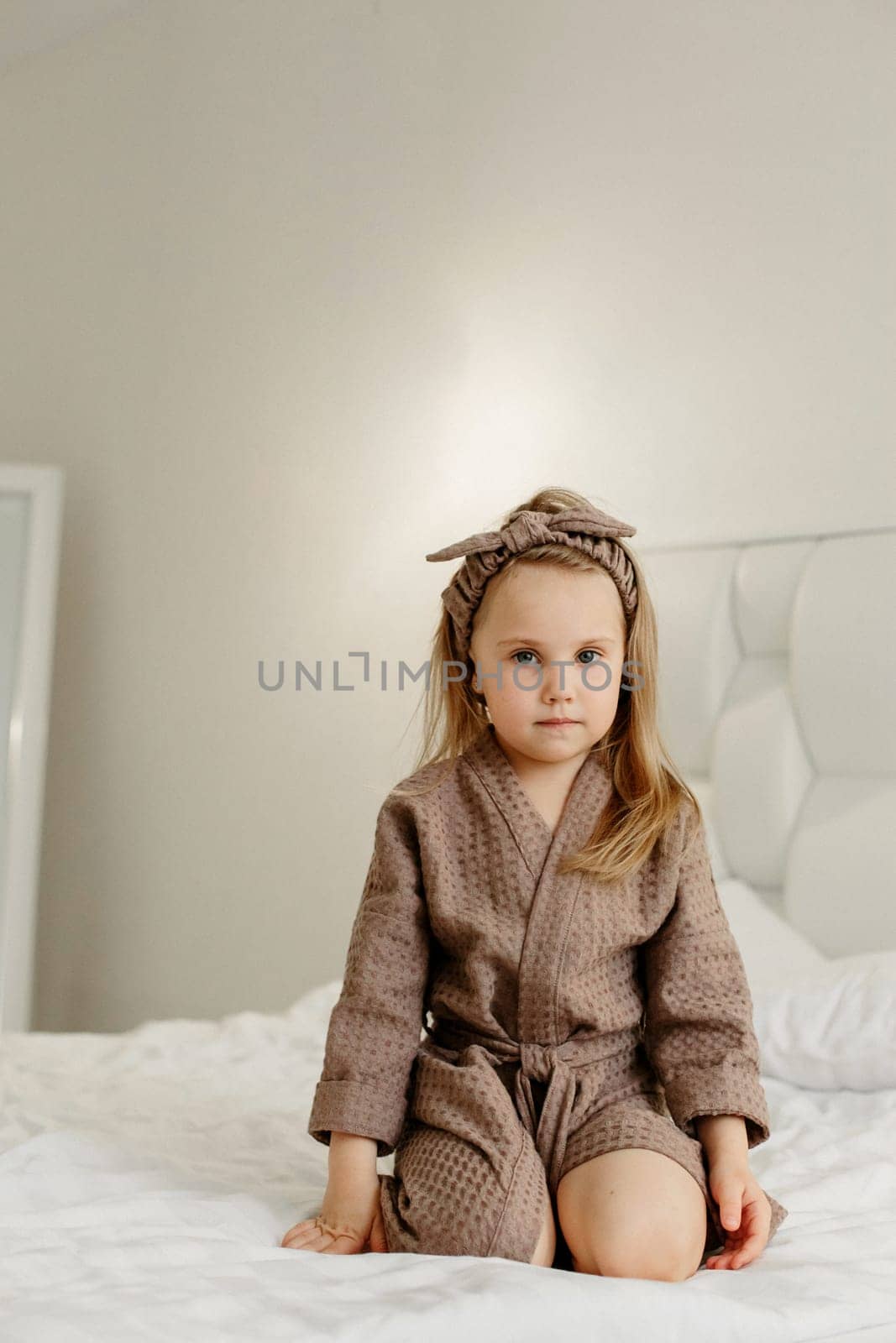 Portrait of a young girl who is sitting in a brown bathrobe on the bed.