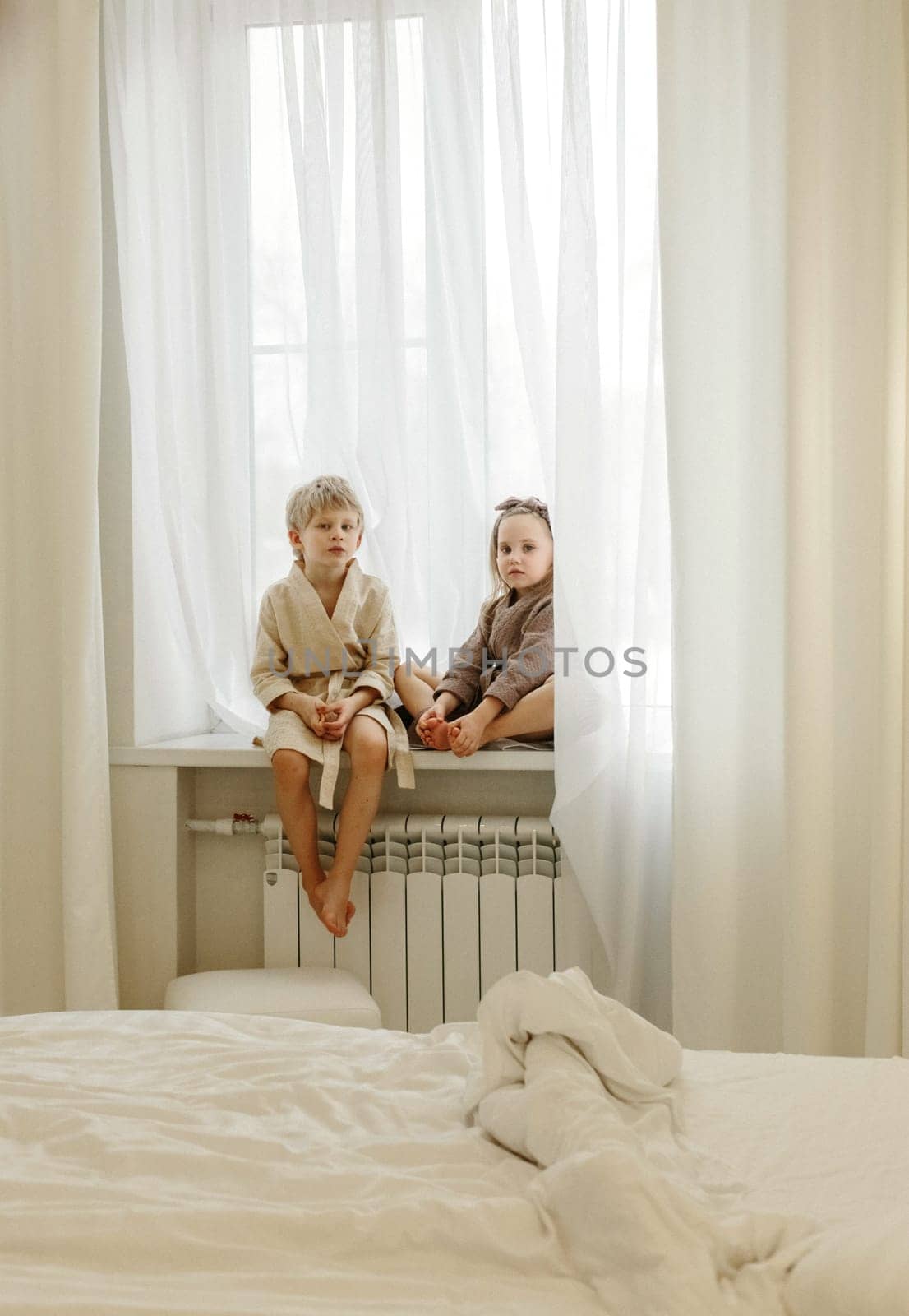 A boy and a girl in bathrobes are sitting on the windowsill, talking, playing.