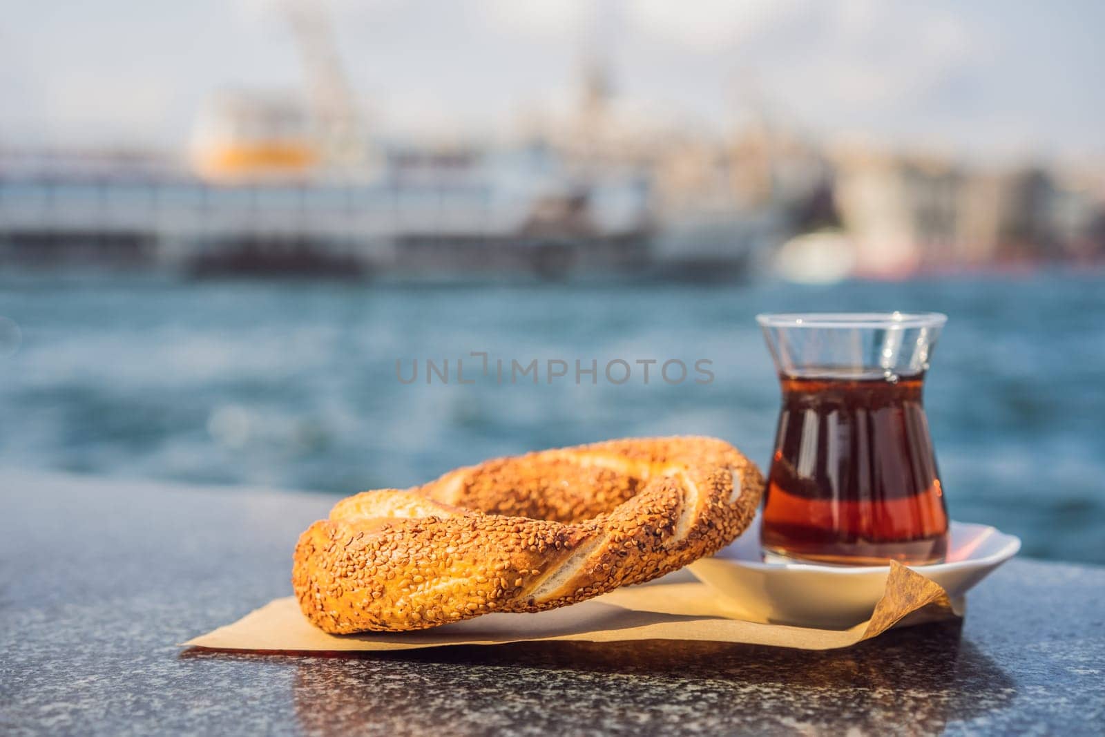 A glass of Turkish tea and bagel Simit against golden horn bay in Istanbul, Turkey. Turkiye by galitskaya